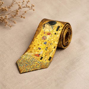 Könnte beinhalten: Eine aufgerollte Krawatte mit einem gold-gelben Design, das an ein Gemälde erinnert. Die Krawatte zeigt ein detailliertes Muster mit verschiedenen Formen und Farben, darunter rote, blaue und schwarze Akzente. Das Design hat eine künstlerische und klassische Ausstrahlung.