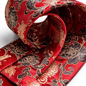 Pode incluir: Close-up de uma gravata vermelha com um intrincado padr&atilde;o floral em ouro e preto. A gravata est&aacute; dobrada, revelando o design detalhado do tecido. A gravata de seda tem um brilho luxuoso, perfeita para ocasi&otilde;es formais.