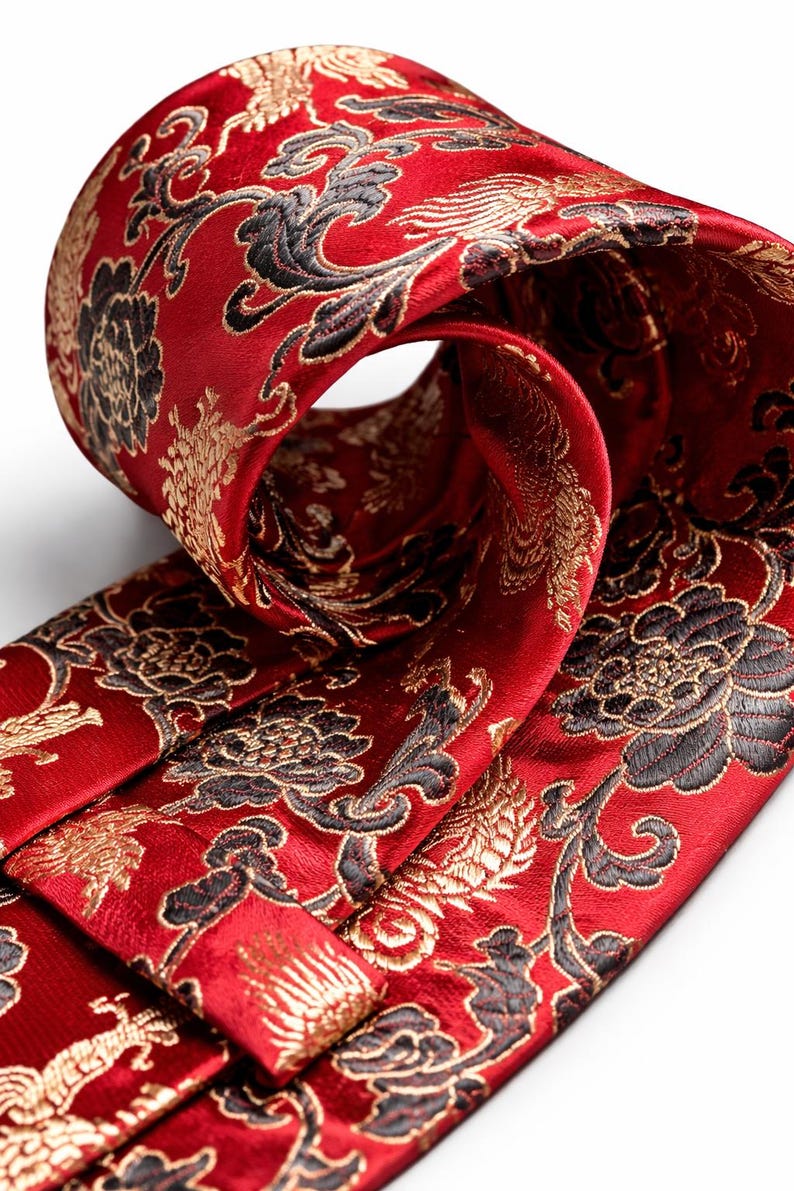 Pode incluir: Close-up de uma gravata vermelha com um intrincado padr&atilde;o floral em ouro e preto. A gravata est&aacute; dobrada, revelando o design detalhado do tecido. A gravata de seda tem um brilho luxuoso, perfeita para ocasi&otilde;es formais.