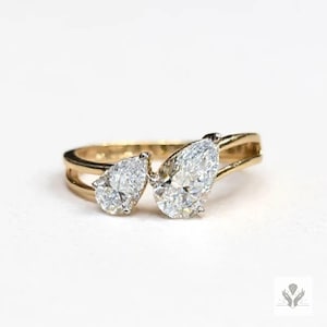 May include: A gold ring featuring two pear-shaped diamonds. The diamonds are set side-by-side, creating a unique and elegant design. The ring has a polished gold band.