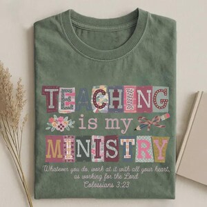 May include: Sage green t-shirt with the words "TEACHING is my MINISTRY" in colorful, patchwork-style letters. The shirt also features a floral design and a pencil with a bow. The text "Whatever you do, work at it with all your heart, as working for the Lord Colossians 3:23" is printed below.