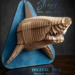 Pode incluir: Escultura de tubarão em madeira montada numa base triangular azul. O tubarão é construído a partir de peças de madeira em camadas, mostrando a sua forma e dentes. O texto na imagem diz "Shark" e "DIGITAL FILE Instant Download".