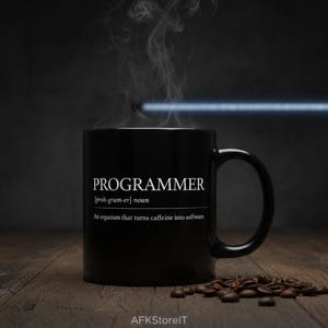 Può includere: Una tazza da caffè nera con la scritta "PROGRAMMER" in bianco e una definizione. Il vapore sale dalla tazza e i chicchi di caffè sono sparsi su una superficie di legno. Un regalo a tema caffè.