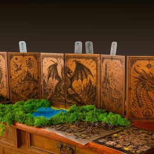 May include: A six-panel wooden dungeon master screen featuring laser-engraved illustrations of dragons, castles, and mountains. The screen includes small vertical tabs at the top and is displayed with green moss and game maps.