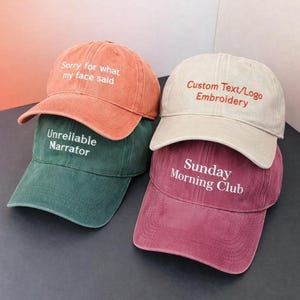 May include: Four baseball caps in orange, green, beige, and burgundy. Each cap has embroidered text: "Sorry for what my face said," "Unreliable Narrator," "Custom Text/Logo Embroidery," and "Sunday Morning Club."