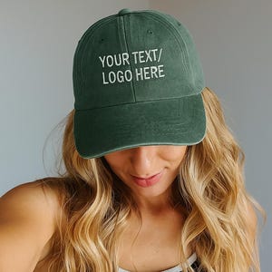 Può includere: Cappellino da baseball verde scuro con la scritta "YOUR TEXT/ LOGO HERE" ricamata in bianco. Il cappellino ha una visiera curva e un aspetto invecchiato. La persona indossa il cappellino con lunghi capelli biondi ondulati.