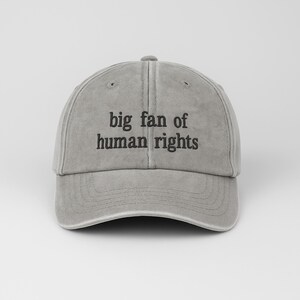 May include: A gray baseball cap with the text "big fan of human rights" in black. The cap has a curved brim and an adjustable strap at the back. The hat is made of a soft, worn material.