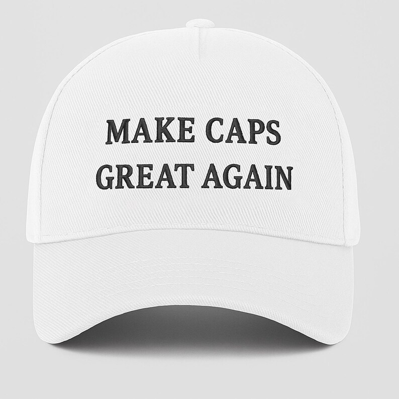 May include: White baseball cap with the text "MAKE CAPS GREAT AGAIN" in black block letters. The cap has a curved brim and a button on top. The hat is made of a textured fabric.