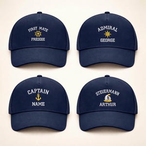 Könnte beinhalten: Vier marineblaue Baseballkappen mit nautischer Stickerei. Jede Kappe zeigt einen anderen Titel: "First Mate", "Admiral", "Captain" und "Steuermann", zusammen mit einem Namen. Die Stickerei ist in Weiß und Gold gehalten.