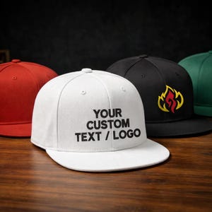 Puede incluir: Una gorra de béisbol blanca con visera plana y el texto negro YOUR CUSTOM TEXT / LOGO impreso en la parte frontal. La gorra está rodeada por otras gorras de béisbol en rojo, negro con un logotipo de llama amarilla y roja, y verde, todas con visera plana.