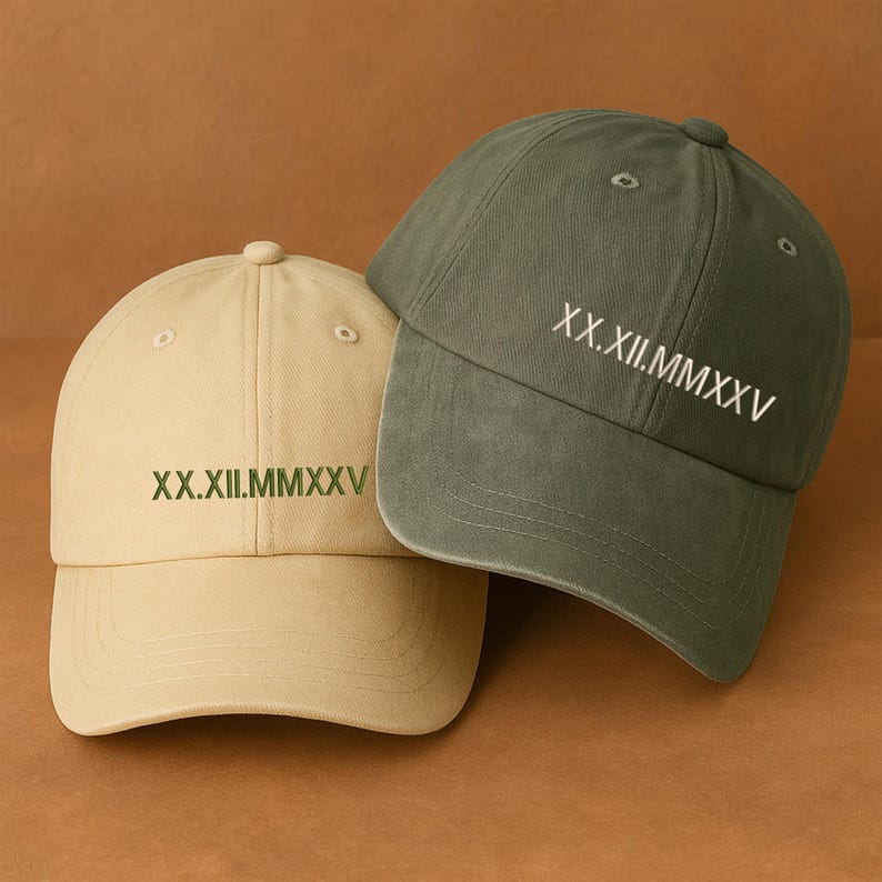May include: Two baseball caps, one tan and one olive green, are displayed. Each cap has the Roman numeral date "XX.XII.MMXXV" embroidered on the front. The caps are made of a soft fabric and have a classic, casual style.