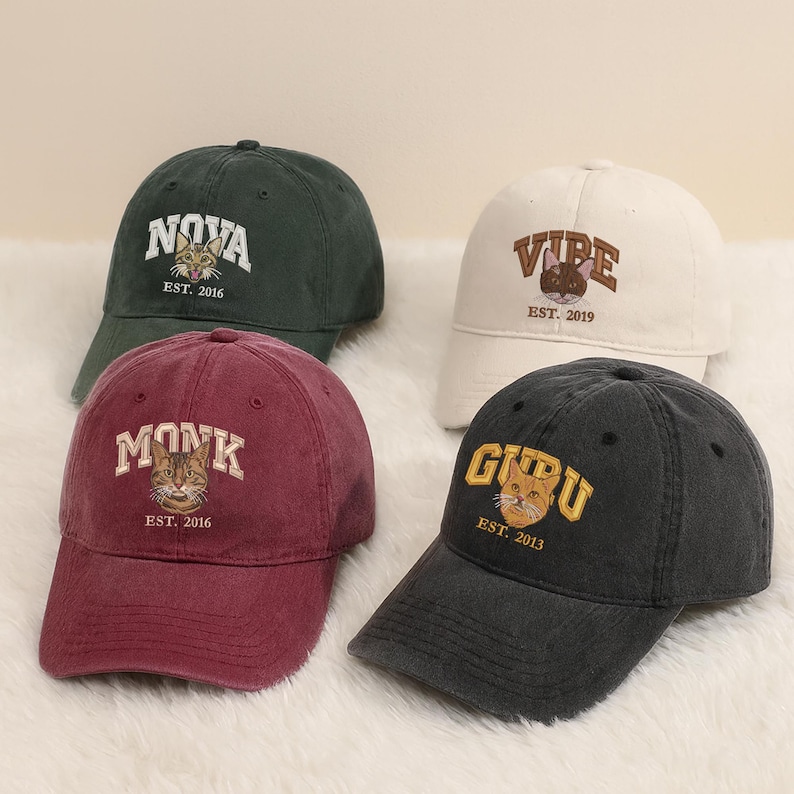 May include: Four baseball caps in different colours: dark green, white, burgundy, and charcoal. Each cap has embroidered text and a cat graphic. The text includes the words "NOVA", "VIBE", "MONK", and "GURU", along with the year of establishment.