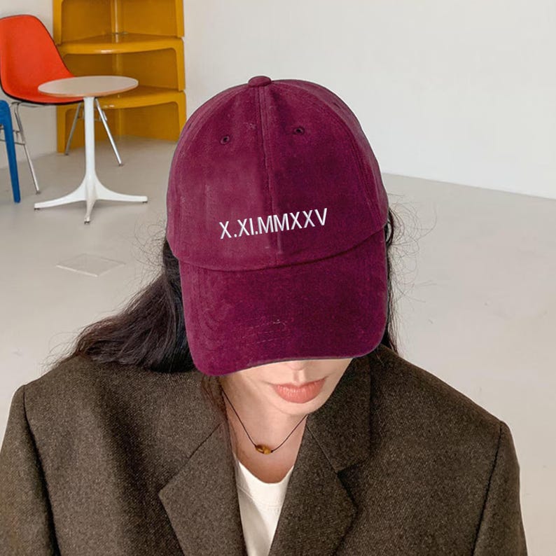 May include: A burgundy baseball cap with the text "X.XI.MMXXV" embroidered in white. The cap is made of a soft material and has a curved brim. The cap is a deep red color.