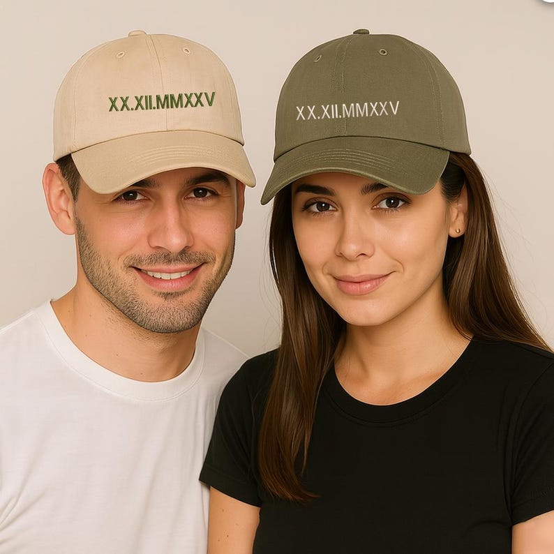 May include: Two baseball caps, one tan and one olive green, each with the Roman numeral text "XX.XII.MMXXV" embroidered on the front. The tan cap is worn by a person wearing a white t-shirt, and the olive green cap is worn by a person wearing a black t-shirt.