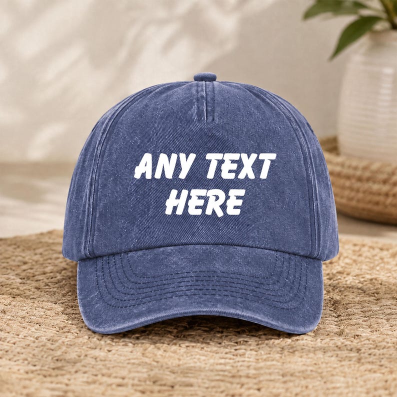 Puede incluir: Una gorra de b&eacute;isbol azul con un acabado desgastado y lavado. La parte frontal de la gorra presenta el texto blanco "ANY TEXT HERE" impreso en una fuente negrita sin remates. La gorra tiene una corona estructurada, visera curva y un bot&oacute;n.