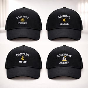May include: Four black baseball caps with nautical-themed designs. Each cap features white and gold text with phrases like "FIRST MATE" and "CAPTAIN", along with personalized names. The caps have a classic, curved brim.