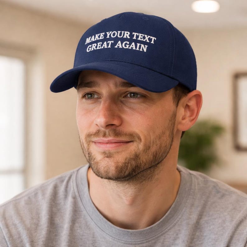 May include: A navy blue baseball cap with the text "MAKE YOUR TEXT GREAT AGAIN" in white. The cap has a curved brim and is worn by a person wearing a gray t-shirt.