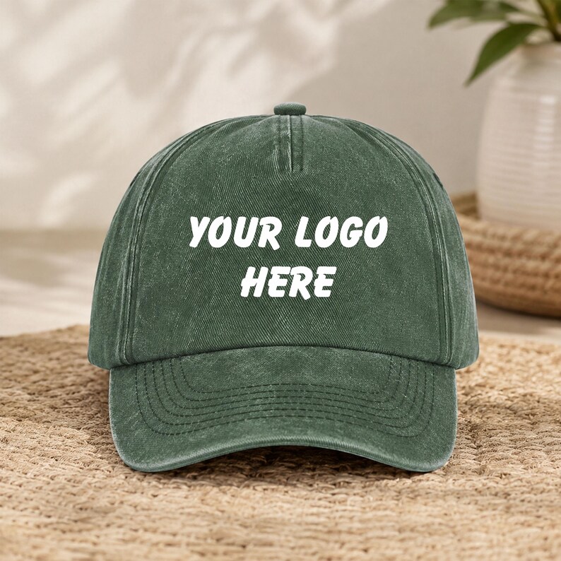 Puede incluir: Una gorra de b&eacute;isbol verde bosque con una textura desgastada y lavada. El panel frontal presenta el texto blanco "YOUR LOGO HERE" impreso en una fuente negrita sin remates. La gorra tiene una corona estructurada, una visera curva y un bot&oacute;n.