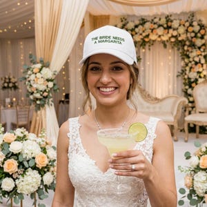Może przedstawiać: Biała czapka z daszkiem z wyhaftowanym na zielono napisem THE BRIDE NEEDS A MARGARITA z przodu. Czapka posiada usztywnianą koronę, zakrzywiony daszek oraz regulowany pasek z tyłu, co zapewnia wygodę podczas noszenia w luźnych stylizacjach.