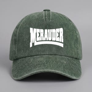 Puede incluir: Una gorra de b&eacute;isbol verde bosque con una textura lavada y desgastada. El panel frontal presenta la palabra MERAUDER impresa en letras may&uacute;sculas blancas y negritas con una ligera curva. La gorra tiene una visera curva y una corona estructurada.