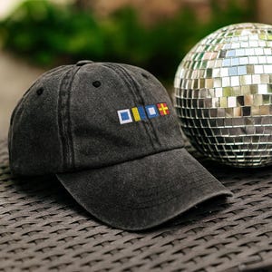 May include: A dark gray baseball cap with a curved brim. The cap features a colorful embroidered design on the front, with a disco ball in the background. The cap is made of a soft, worn material.