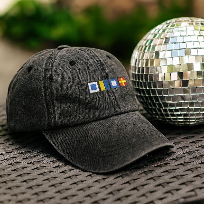 May include: A dark gray baseball cap with a curved brim. The cap features a colorful embroidered design on the front, with a disco ball in the background. The cap is made of a soft, worn material.
