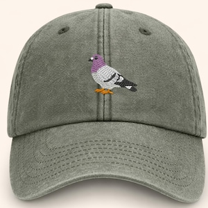 May include: A green baseball cap with a curved brim. The cap features an embroidered pigeon with purple, gray, black, and orange details. The cap has a six-panel design with a button on top.