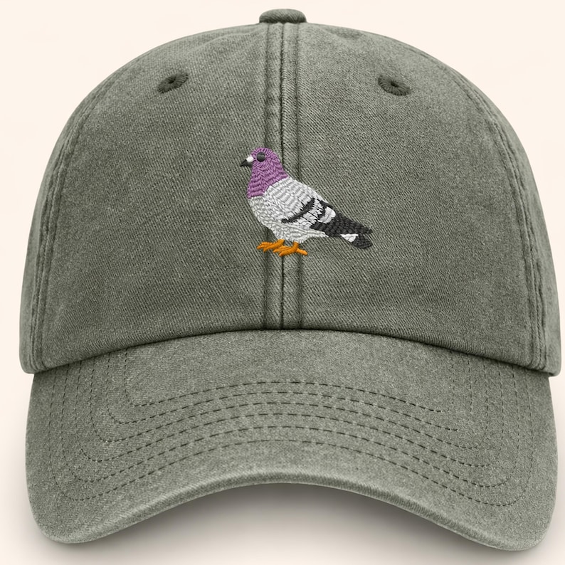May include: A green baseball cap with a curved brim. The cap features an embroidered pigeon with purple, gray, black, and orange details. The cap has a six-panel design with a button on top.