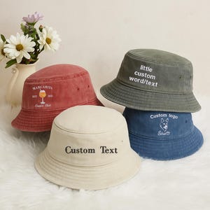 May include: Four bucket hats in various colors: red, cream, olive green, and blue. The red hat has "MARGARITA" and "Cousins Club" text. The cream hat says "Custom Text". The green hat says "little custom word/text". The blue hat has a dog logo.