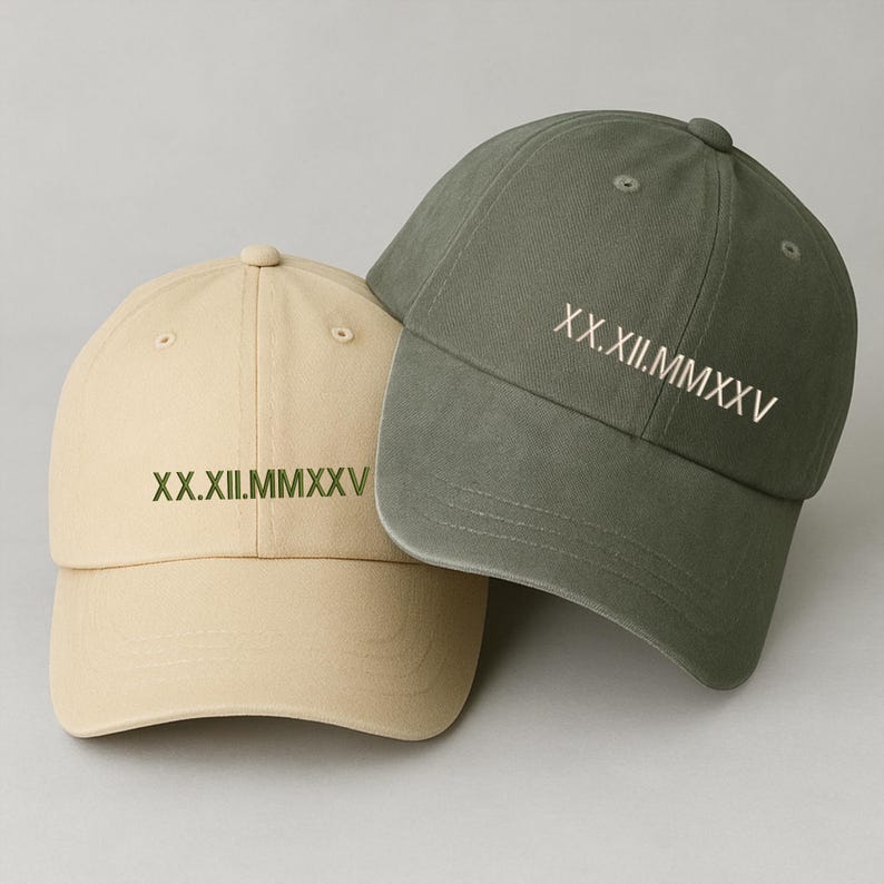 May include: Two baseball caps, one beige and one olive green, are displayed. Each cap has the Roman numeral date "XX.XII.MMXXV" embroidered on the front. The caps are made of a soft fabric and have a classic, curved brim.