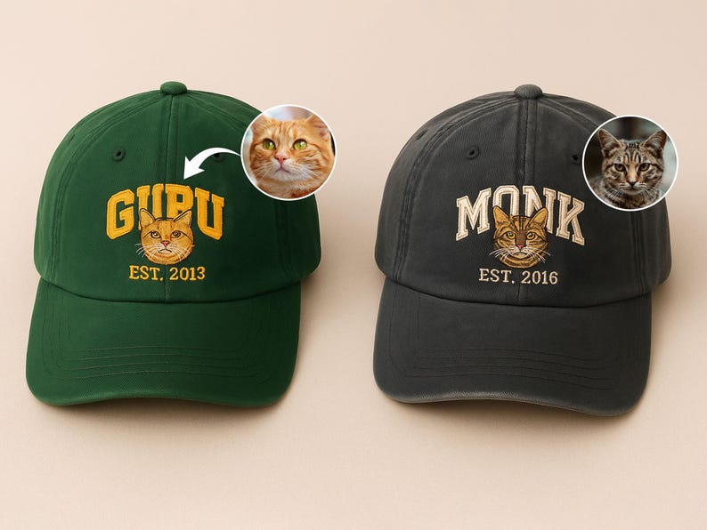 May include: Two baseball caps, one dark green and one charcoal grey. The green cap has "GURU" and "EST. 2013" embroidered with a cat face graphic. The grey cap has "MONK" and "EST. 2016" with a cat face graphic.