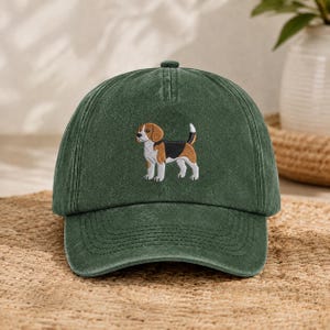 May include: A forest green baseball cap featuring an embroidered beagle dog on the front panel. The dog is depicted in profile with brown, black, and white fur, standing with its tail pointed upward. The cap has a structured crown and a curved brim.