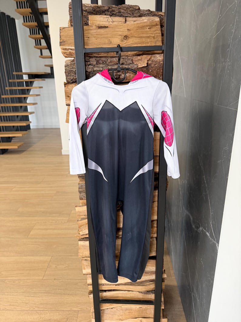 May include: A white ceramic mug with a black handle and the text "But First, Coffee" in a bold, black font. The mug is set against a blurred background. The mug appears to be approximately 10 cm tall.