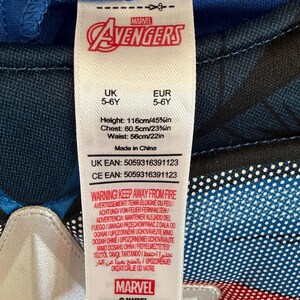 May include: A white clothing tag attached to a blue and black Marvel Avengers garment. The tag displays the Marvel logo, size 5-6Y, height 116cm/45.5in, chest 60.5cm/23.75in, waist 56cm/22in, Made in China, and a multi-language fire safety warning.