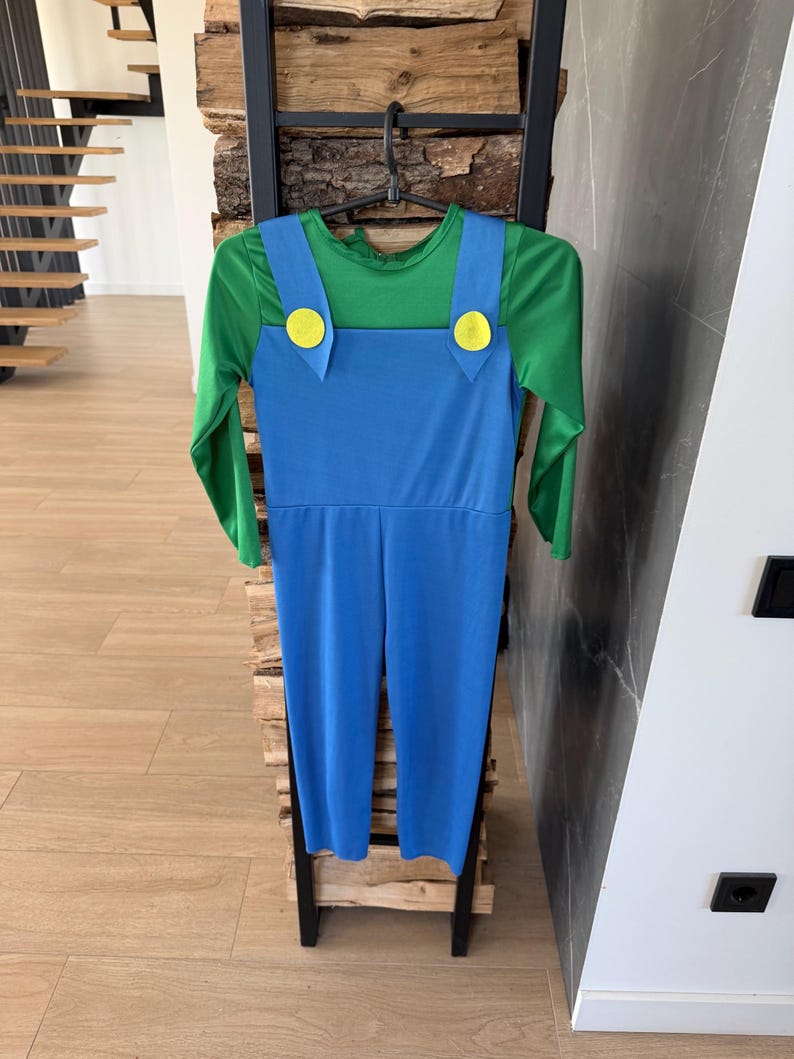 May include: A long-sleeved jumpsuit featuring a bright green shirt top integrated with blue overalls. The blue overalls have two large, round, yellow buttons attached at the front where the straps meet the chest piece, creating a classic character look.