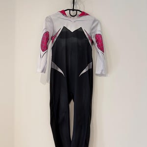 May include: A Spider-Gwen costume, a black and white jumpsuit with pink detailing on the shoulders and hood. The costume has a spiderweb pattern on the shoulders and is hanging on a black hanger.