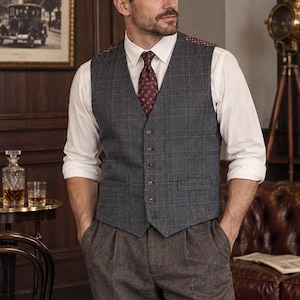 Puede incluir: Un chaleco de cuadros gris carbón con cinco botones, usado sobre una camisa blanca de manga larga con una corbata estampada de color rojo oscuro. El conjunto incluye pantalones de tweed marrón y una gorra plana gris carbón a juego.