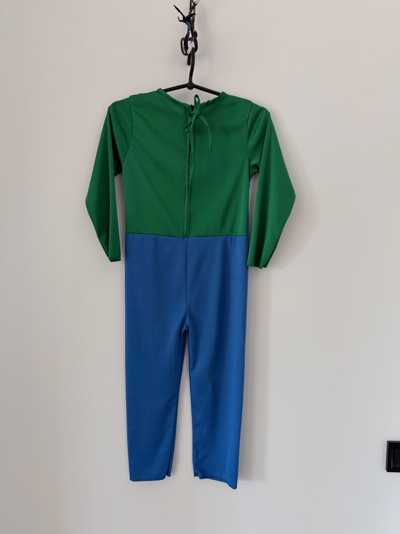 May include: A long-sleeved jumpsuit featuring a solid green top section and a solid blue bottom section. The garment has a round neckline with a tie closure at the back of the neck, long sleeves, and full-length pant legs, presented on a hanger.