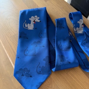 Puede incluir: Tres corbatas azules con un diseño de ratón de dibujos animados. Las corbatas son de un azul brillante, con un patrón repetido de un personaje de ratón en varias poses. Las corbatas parecen estar hechas de una tela suave, posiblemente seda o satén.