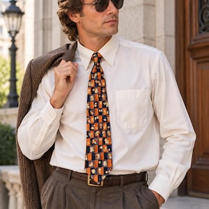 May include: A long-sleeved cream button-down shirt with a chest pocket, paired with a brown leather belt and dark brown trousers. A brown textured blazer is draped over one shoulder. A necktie features a checkered pattern of orange and navy blue.