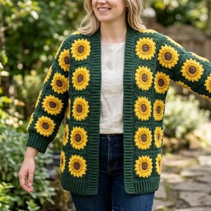 Könnte beinhalten: Ein grüner Häkelcardigan mit Sonnenblumenmuster. Der Cardigan ist dunkelgrün mit gelben und braunen Sonnenblumen. Der offene Cardigan wird über einem weißen Oberteil und einer blauen Jeans getragen. Die Ärmel sind lang und der Cardigan ist knielang.