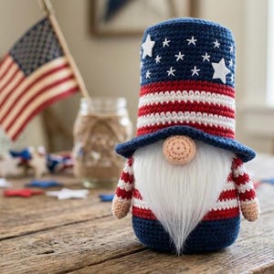 May include: A patriotic gnome doll with a blue, red, and white color scheme. The gnome has a tall hat with white stars on a blue background, red and white striped body, and a long white beard. An American flag is in the background.