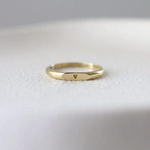 Könnte beinhalten: Ein goldfarbener Ring mit einem kleinen herzförmigen Ausschnitt. Der Ring hat ein schlichtes, elegantes Design und scheint aus Metall zu sein. Der Ring ist glatt und das Herz ist mittig auf der Ringoberfläche platziert.