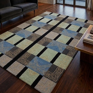 Könnte beinhalten: Ein rechteckiger Teppich mit geometrischem Muster. Der Teppich hat Quadrate in Blau-, Grün-, Grau- und Beigetönen, getrennt durch schwarze Linien. Er liegt auf einem dunklen Holzboden in einem Raum mit großen Fenstern.