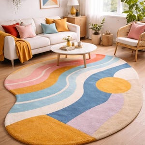 May include: An oval rug with a colourful, wavy design in shades of yellow, orange, pink, blue, and purple. The rug features a large yellow sun-like circle and a yellow rectangular shape. The rug is placed on a wooden floor.