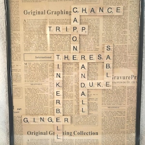 May include: Framed artwork featuring a collage of vintage newspaper clippings. Scrabble tiles spell out phrases like "CHANCE" and "THERE IS A". The artwork is encased in a black frame, creating a unique decorative piece.