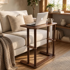 May include: A dark brown wooden C-shaped side table with a rectangular top and a sturdy base. The table features a smooth finish and vertical support legs, designed to slide under furniture. A silver laptop is placed on the flat surface.