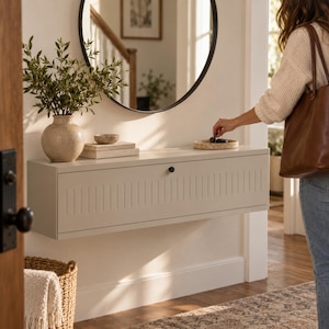 May include: A light beige wall-mounted floating console table featuring a rectangular shape with vertical grooved detailing on the front panel and a single small black circular knob. The console is positioned horizontally on a white wall.