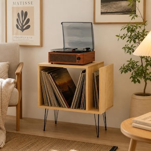 May include: A wooden record player stand with a light wood finish and black metal hairpin legs. The stand features an open storage compartment filled with vinyl records and a top surface holding a brown wooden record player with a clear lid.
