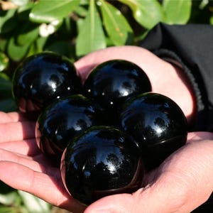 Può includere: Cinque oggetti sferici lisci e levigati con una superficie nera profonda e riflettente. Ogni sfera è uniforme per forma e dimensioni, mostrando una finitura lucida che cattura i riflessi di luce sulla sua parte esterna arrotondata.